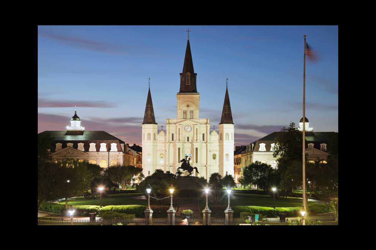St. Louis Cathedral at night with a statue in front, surrounded by trees and buildings.